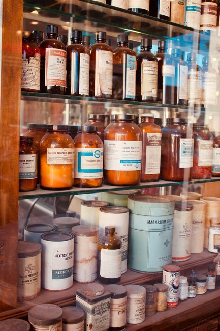 A collection of vintage pharmacy bottles on wooden shelves, showcasing old medicine containers.