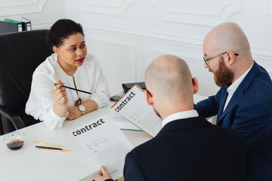 Three business professionals in discussion over a contract in a modern office setting.