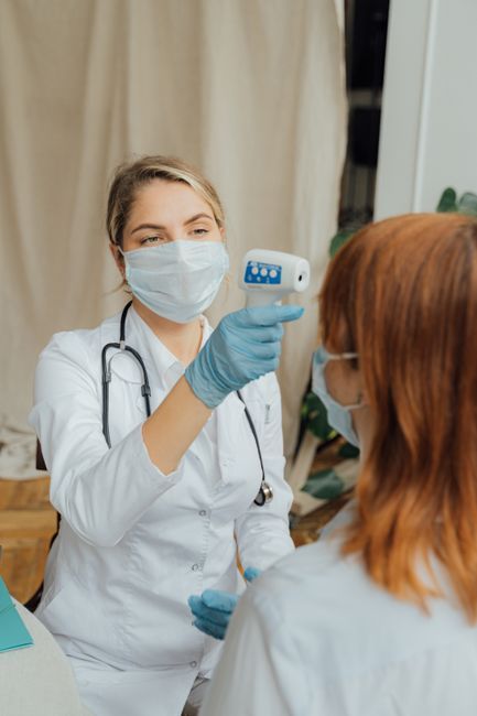 A female doctor uses a thermometer to measure a patient's temperature while wearing PPE.