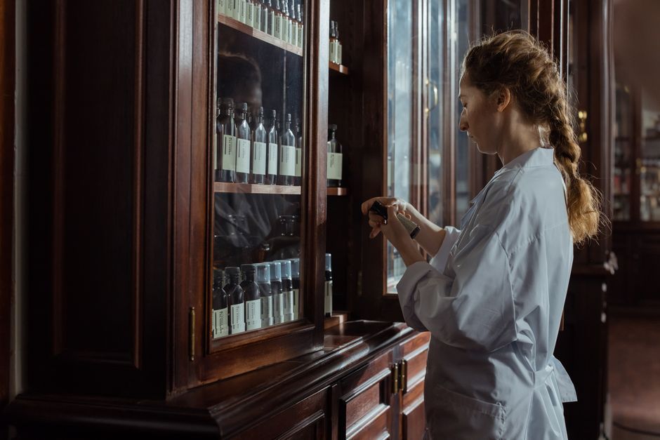 A female pharmacist in a white uniform organizing bottles in a pharmacy cabinet.