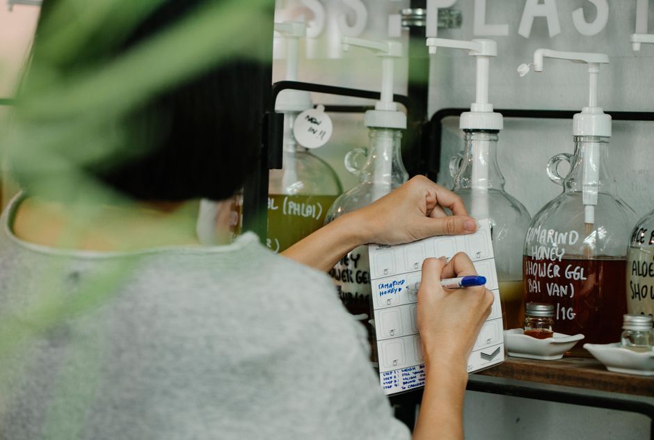 Person using a pen to take notes in an eco-friendly refill store with glass containers.