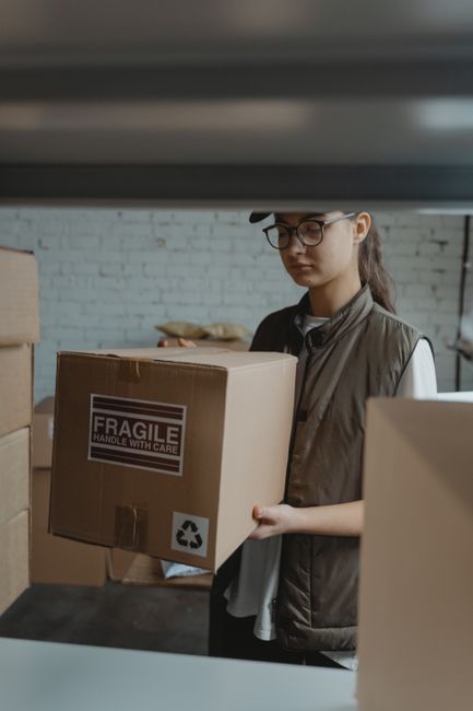 Female courier handling a fragile package in a warehouse setting.