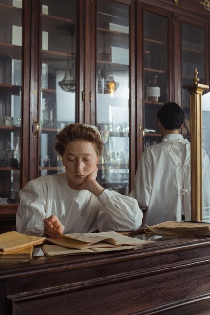 An antique pharmacy with a pharmacist in historical attire reading documents at a wooden counter.