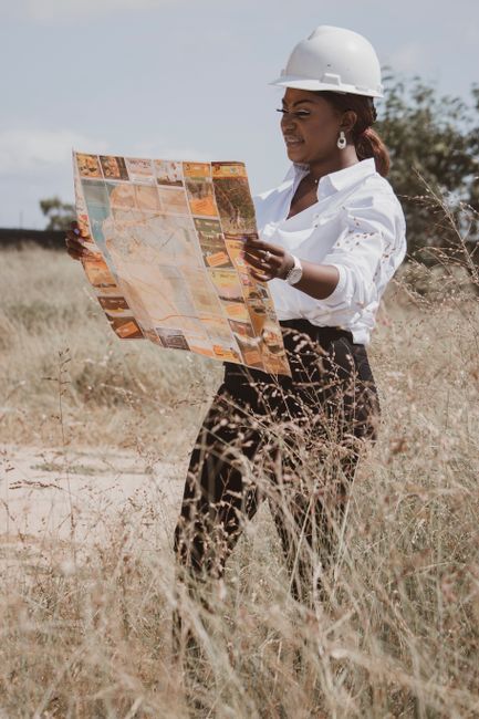 A female engineer in a safety helmet reads a map in a grass field on a sunny day.