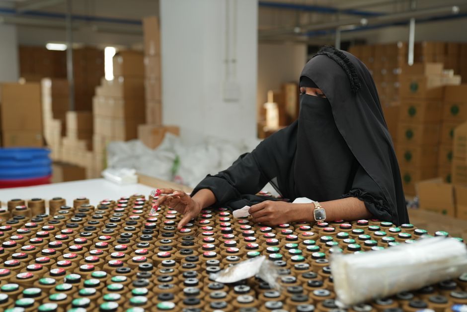 A woman wearing a hijab organizes bottles in a warehouse environment.