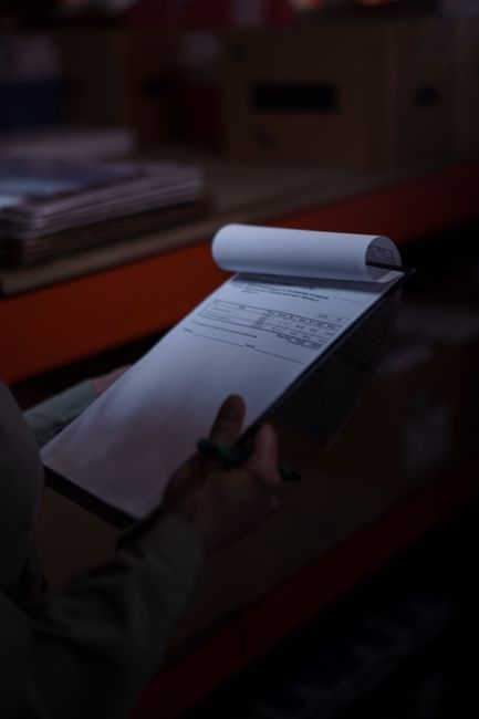 Silhouette of a person holding a clipboard with documents in a dimly lit warehouse.